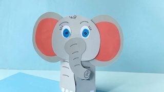 paper elephant with pink ears and blue eyes. light blue background