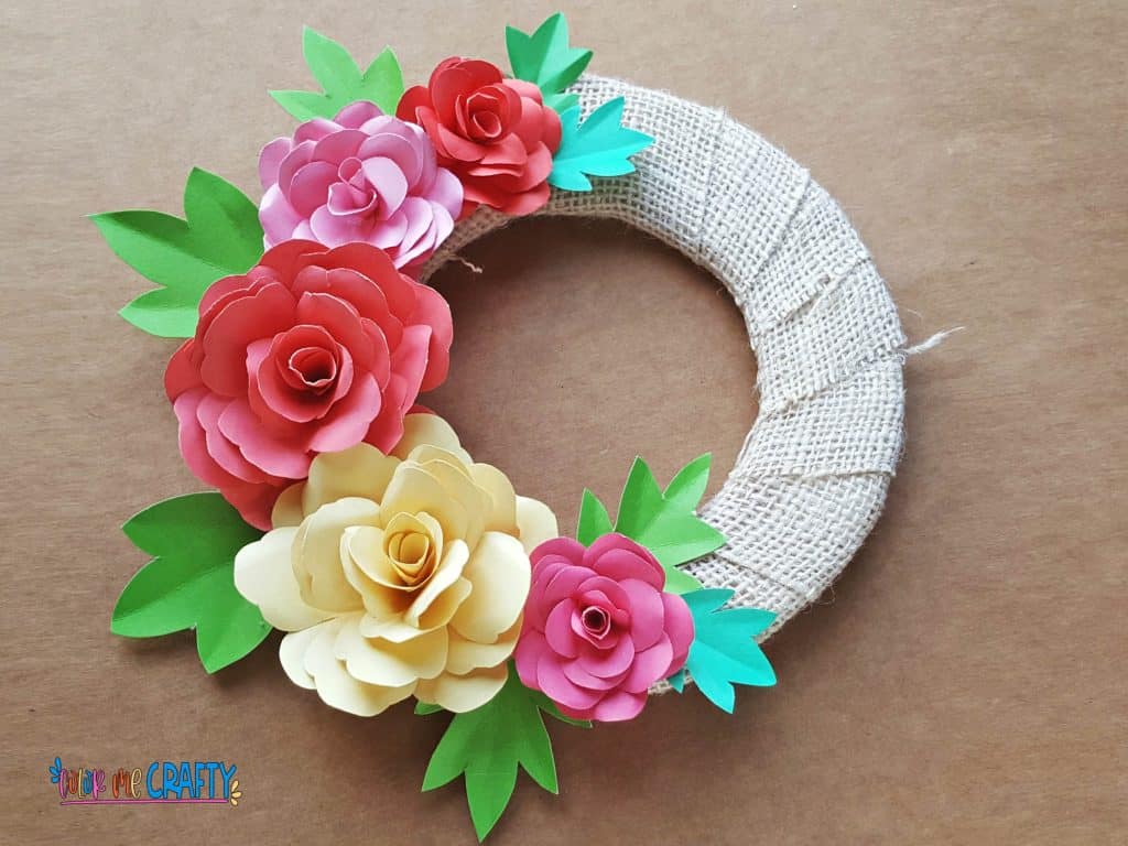 wreath made with burlap and pink yellow and red paper flowers with green leaves on a brown background