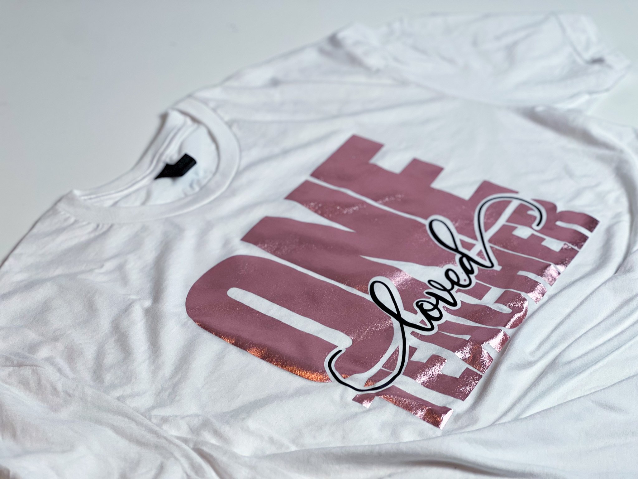 White t-shirt showcasing a vibrant pink and black vinyl design created using Cricut, reading 'ONE loved TEACHER.