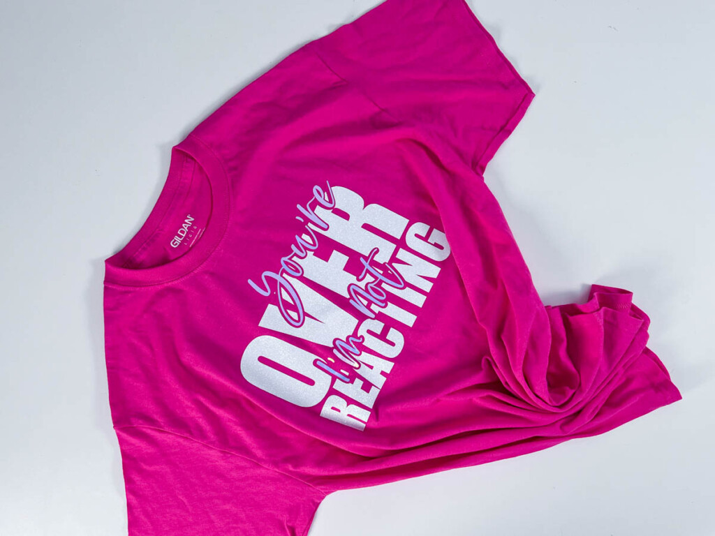 Bright pink Gildan t-shirt with bold white vinyl text design reading “You’re Overreacting I’m not,” laid flat to showcase custom SVG made with Cricut Joy.