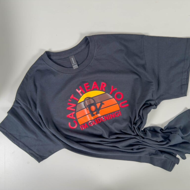 Finished black t-shirt featuring a retro sunset Cricut design with red and orange layers and bold text that reads ‘CAN’T HEAR YOU, I’M GARDENING!