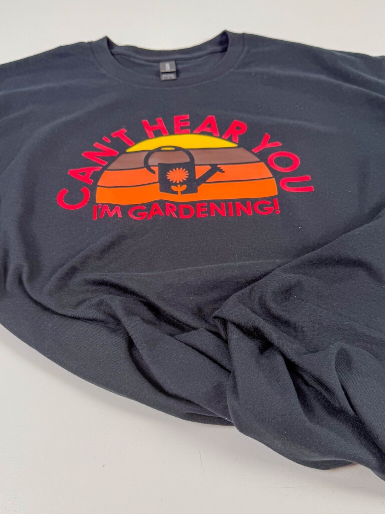 Side angle view of retro sunset Cricut shirt laid flat, showcasing gardening design with watering can and text curved around the sun